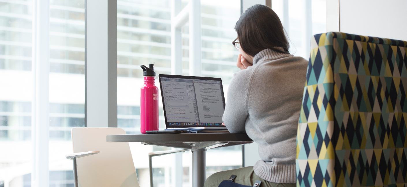 a person studying on a laptop with a pink water bottle beside 