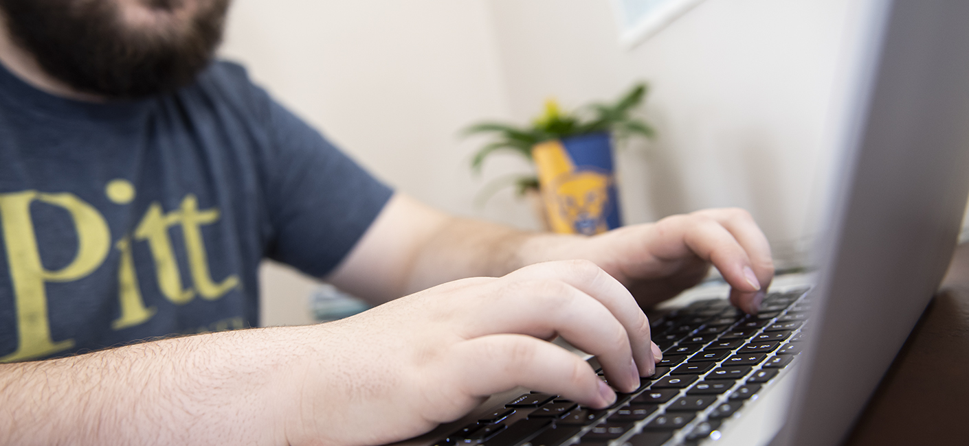 a person typing on a laptop wearing a Pitt shirt