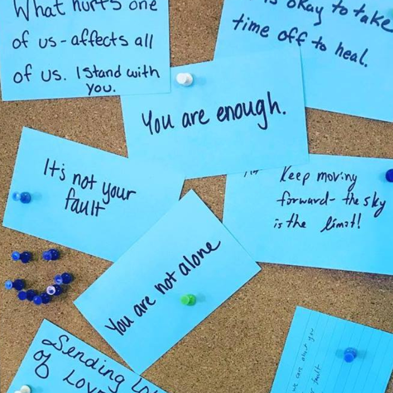 Teal cards with encouraging messages written on them posted to a cork board