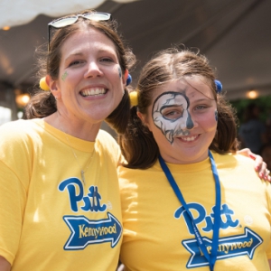 Amy Kleebank with her daughter Amelia at Staff Council's Pitt Day at Kennywood, wearing bright yellow Pitt shirts. Amelia has face painting on her right eye.