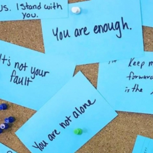 Teal cards with encouraging messages written on them posted to a cork board
