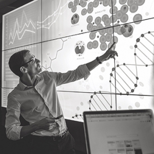 People in a black and white photo looking at and pointing to a screen filled with graphs and images.
